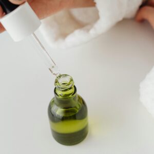 Close-up of hands with manicured nails holding a dropper over a green serum bottle.